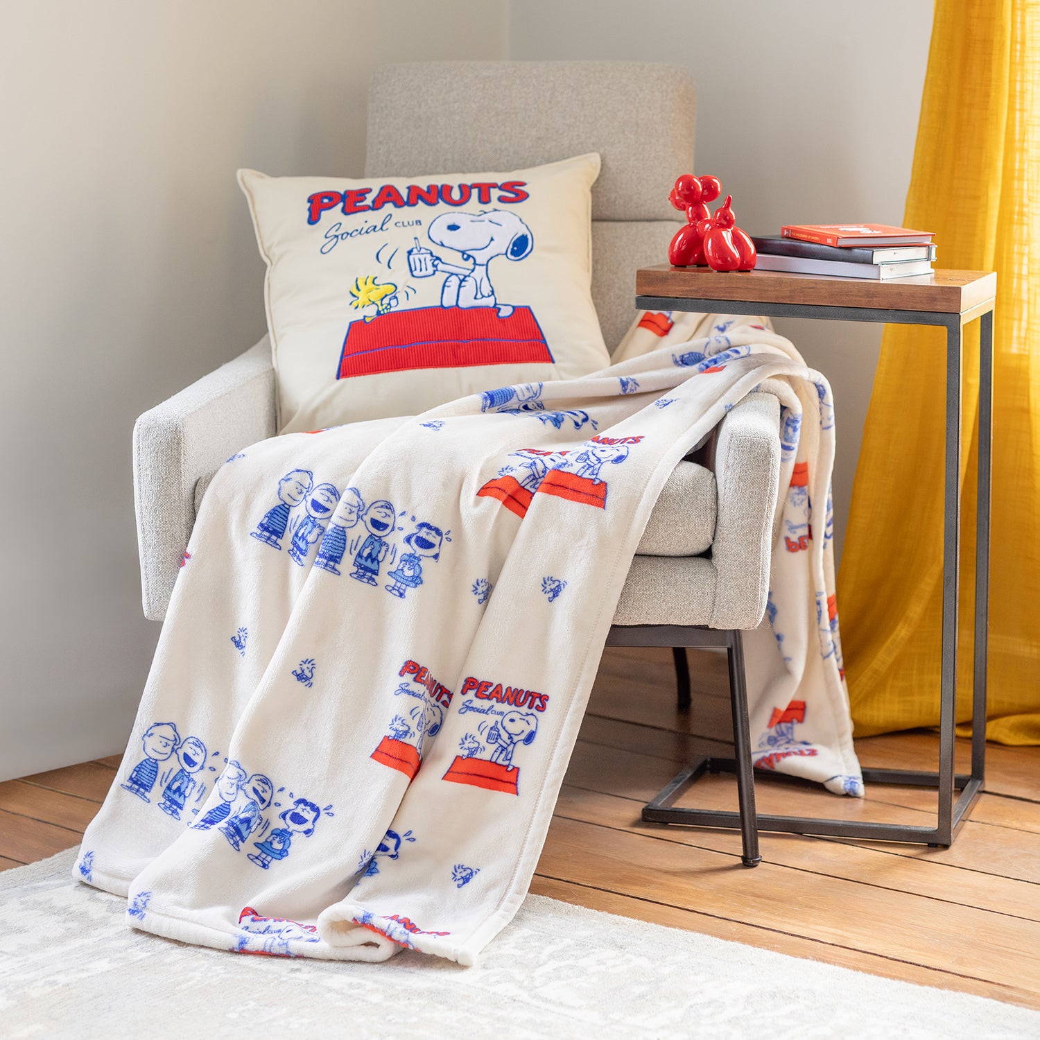 Peanuts social club throw and matching pillow decorated on a grey chair.