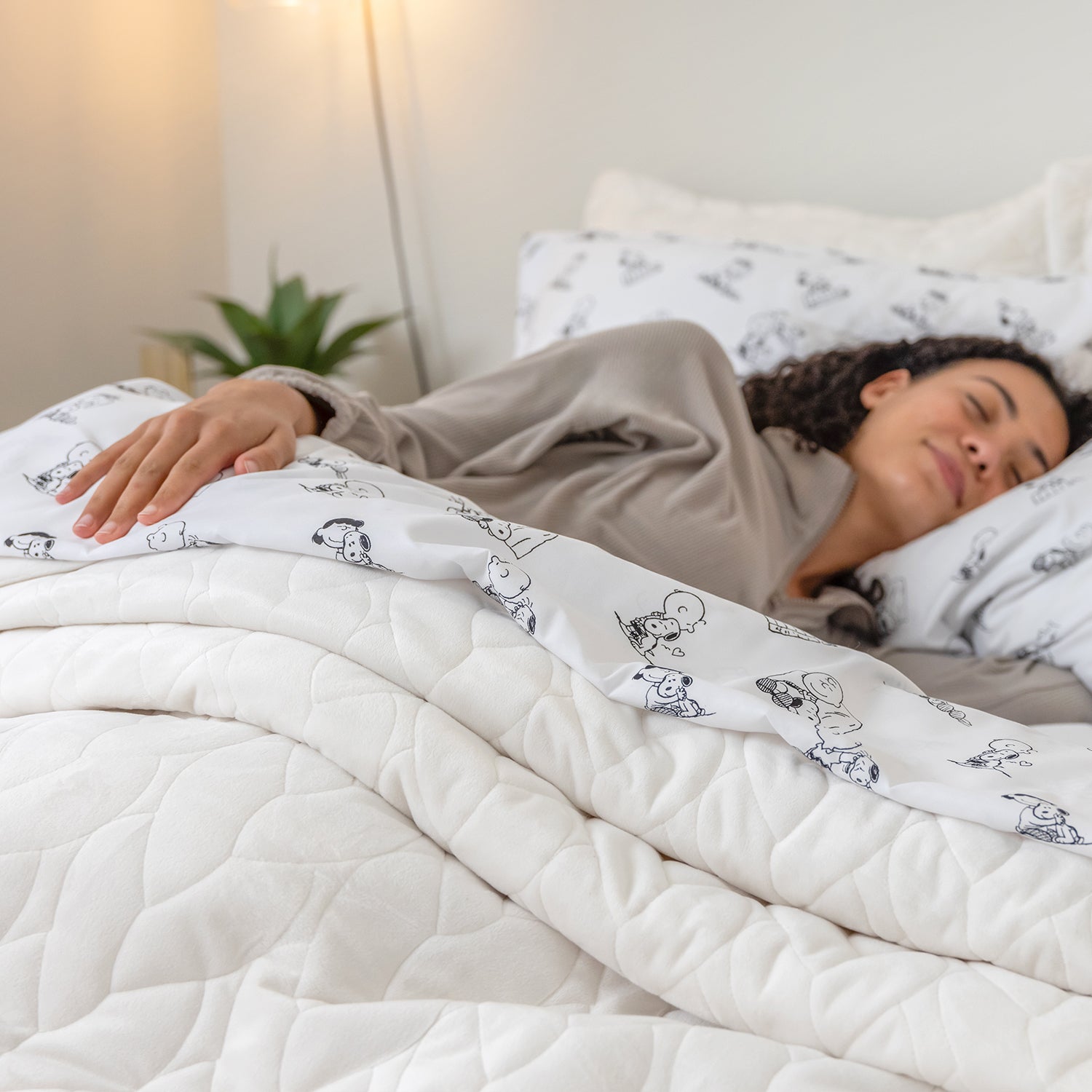 Woman sleeping under a white comforter with cartoon patterns in a cozy bedroom.