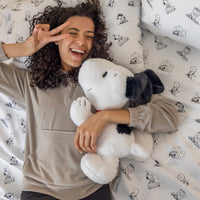 Person holding a Snoopy plush toy on a bed with Snoopy and Woodstock bedding.