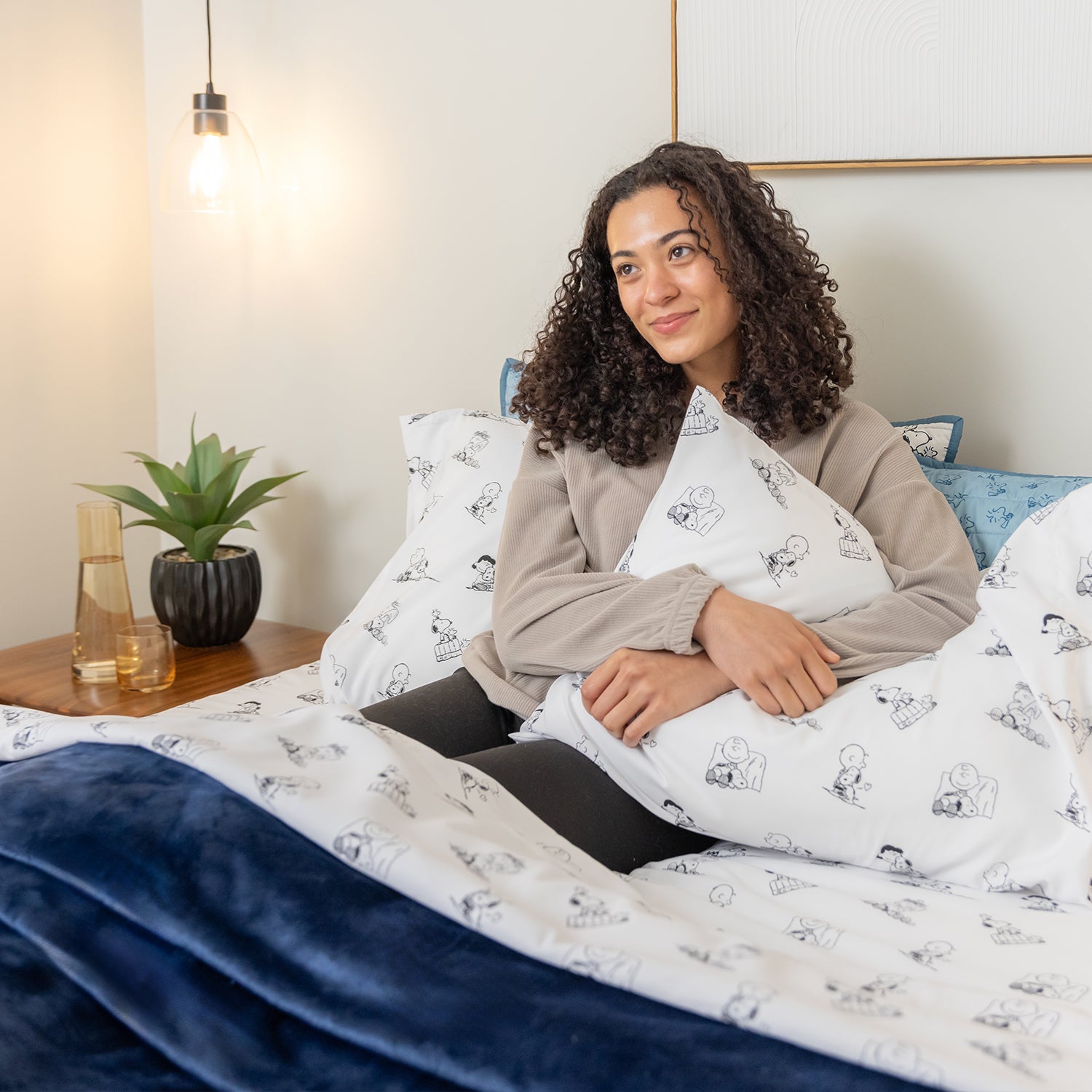 Woman sitting on a bed with Snoopy-themed bedding in a cozy bedroom setting.