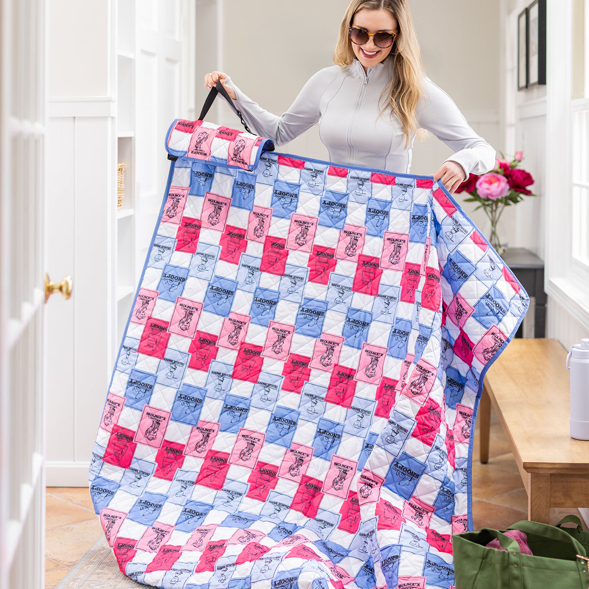 Woman holding a colorful outdoor throw with a checkered pattern in a room.