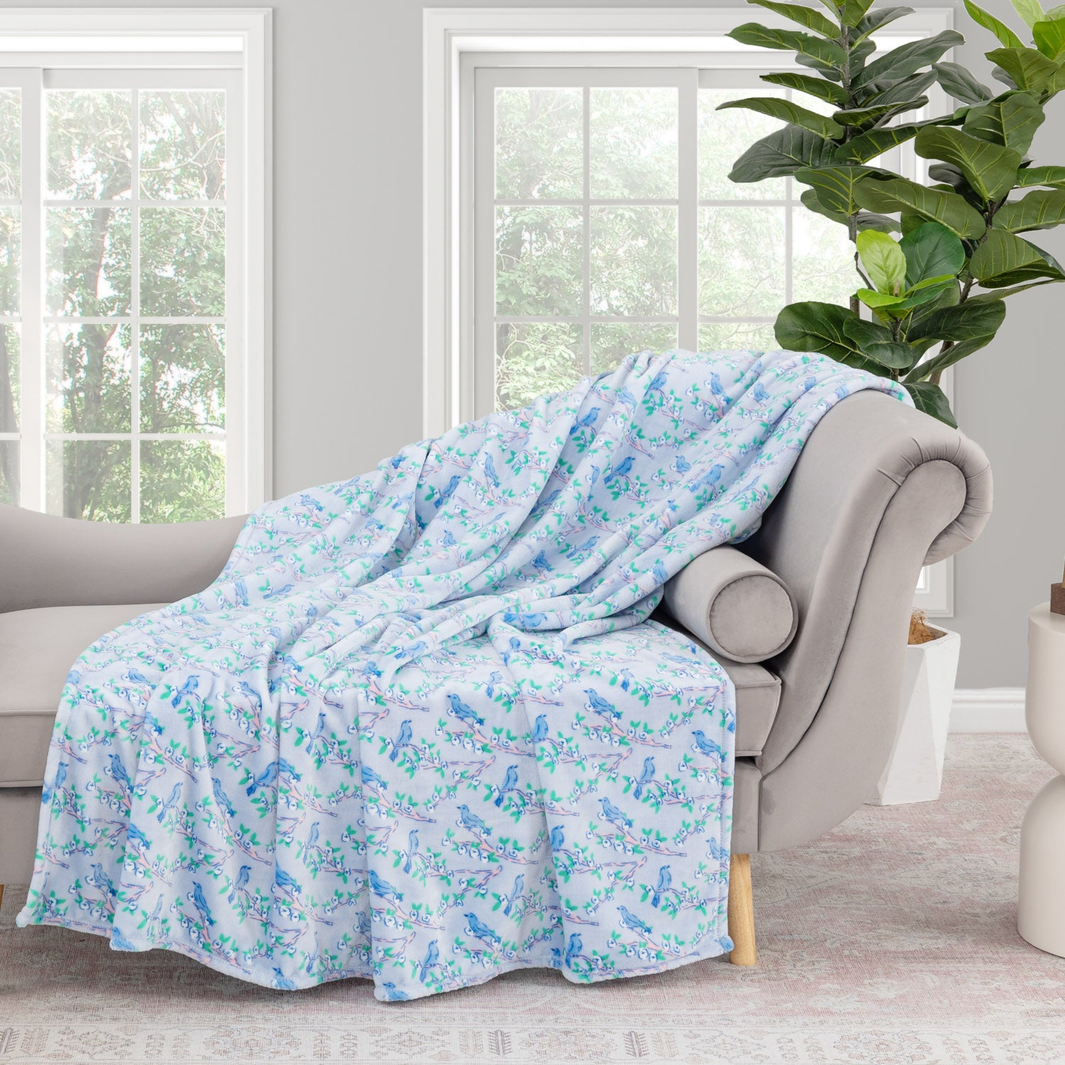 Krissy Mast Artist Series printed cherry blossom print throw draped neatly over a grey sofa in a staged room.