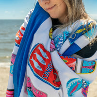 Person wrapped in a colorful towel with fish designs on a beach