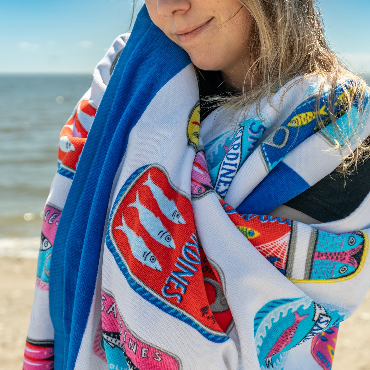 Person wrapped in a colorful towel with fish designs on a beach