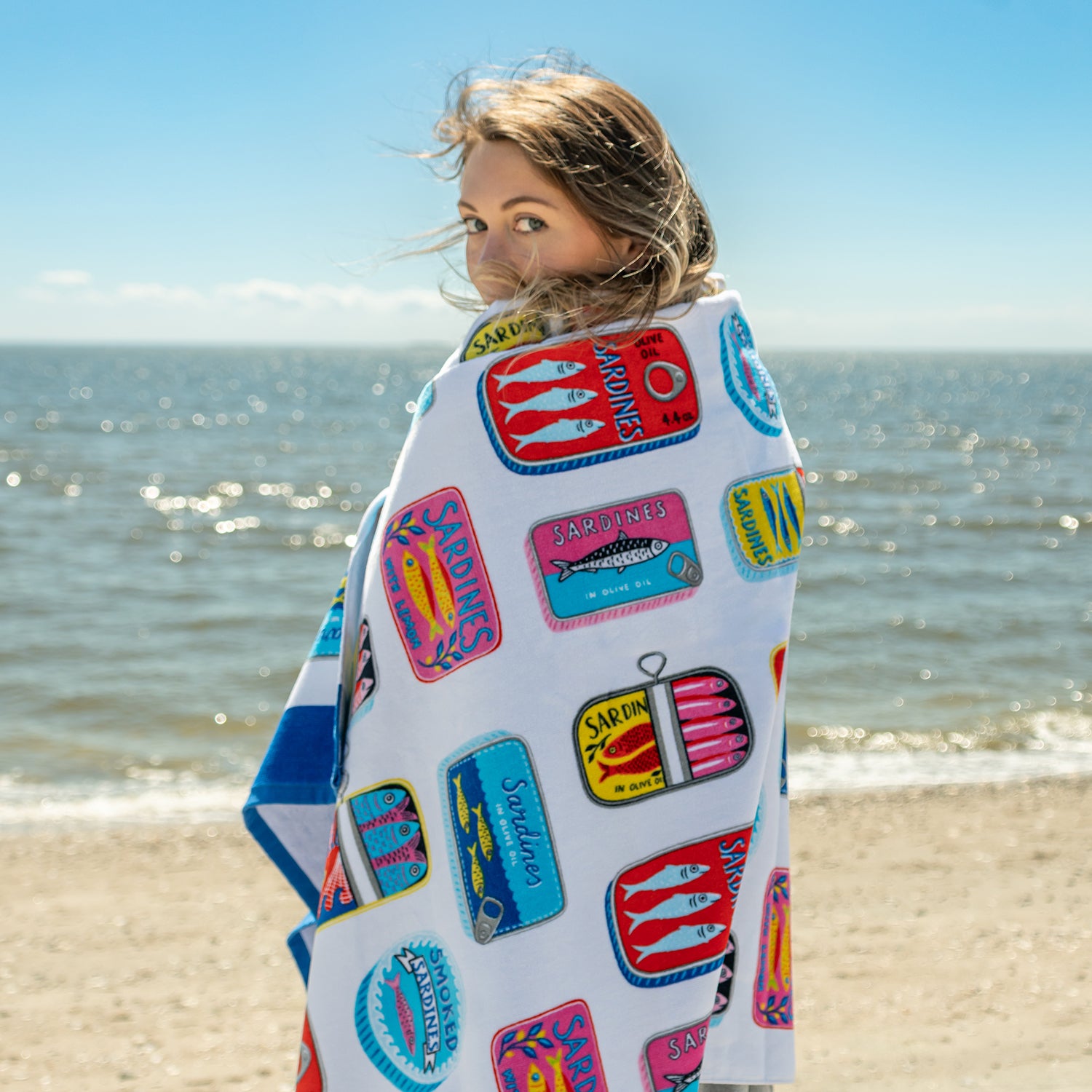 Person wrapped in a colorful towel with patches on a beach