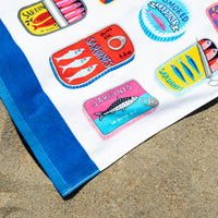 Collection of colorful sardine can-shaped magnets on a blue towel with sand in the background