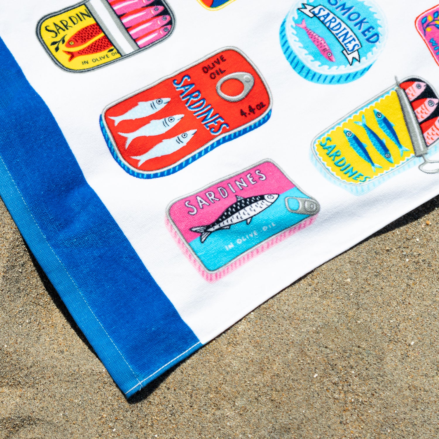 Collection of colorful sardine can-shaped magnets on a blue towel with sand in the background
