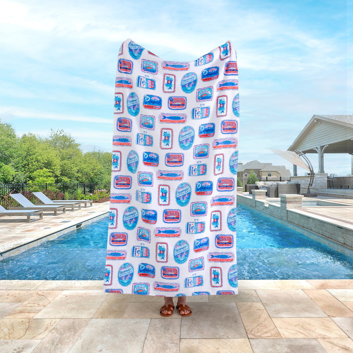 Krissy Mast Sardine printed beach towel held up by a person standing by a pool. 