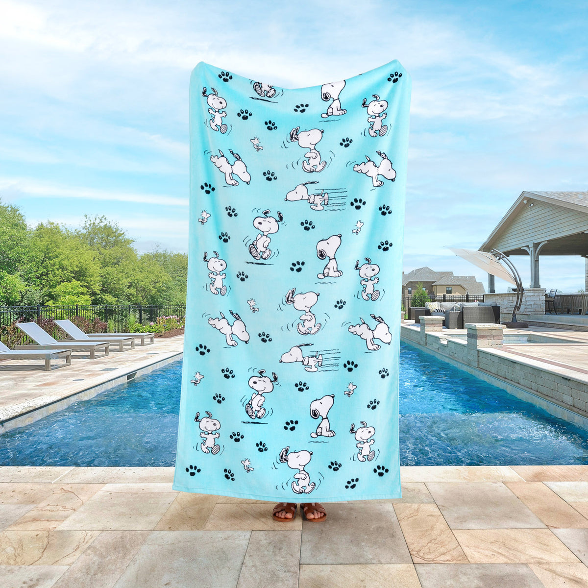 Blue peanuts beach towel held up by a person standing by a pool.
