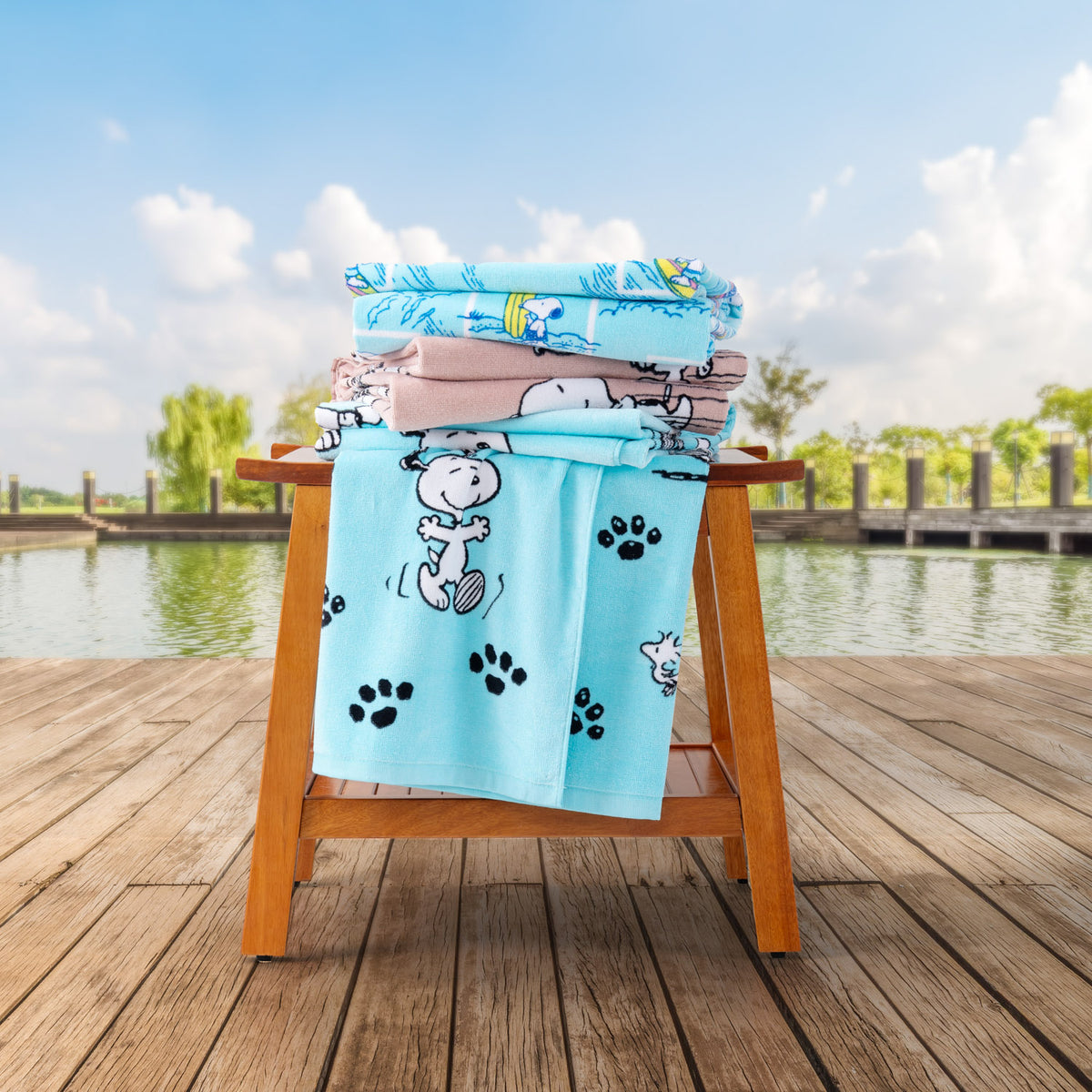 Peanuts beach towels stacked neatly on a wooden chair by a pond.