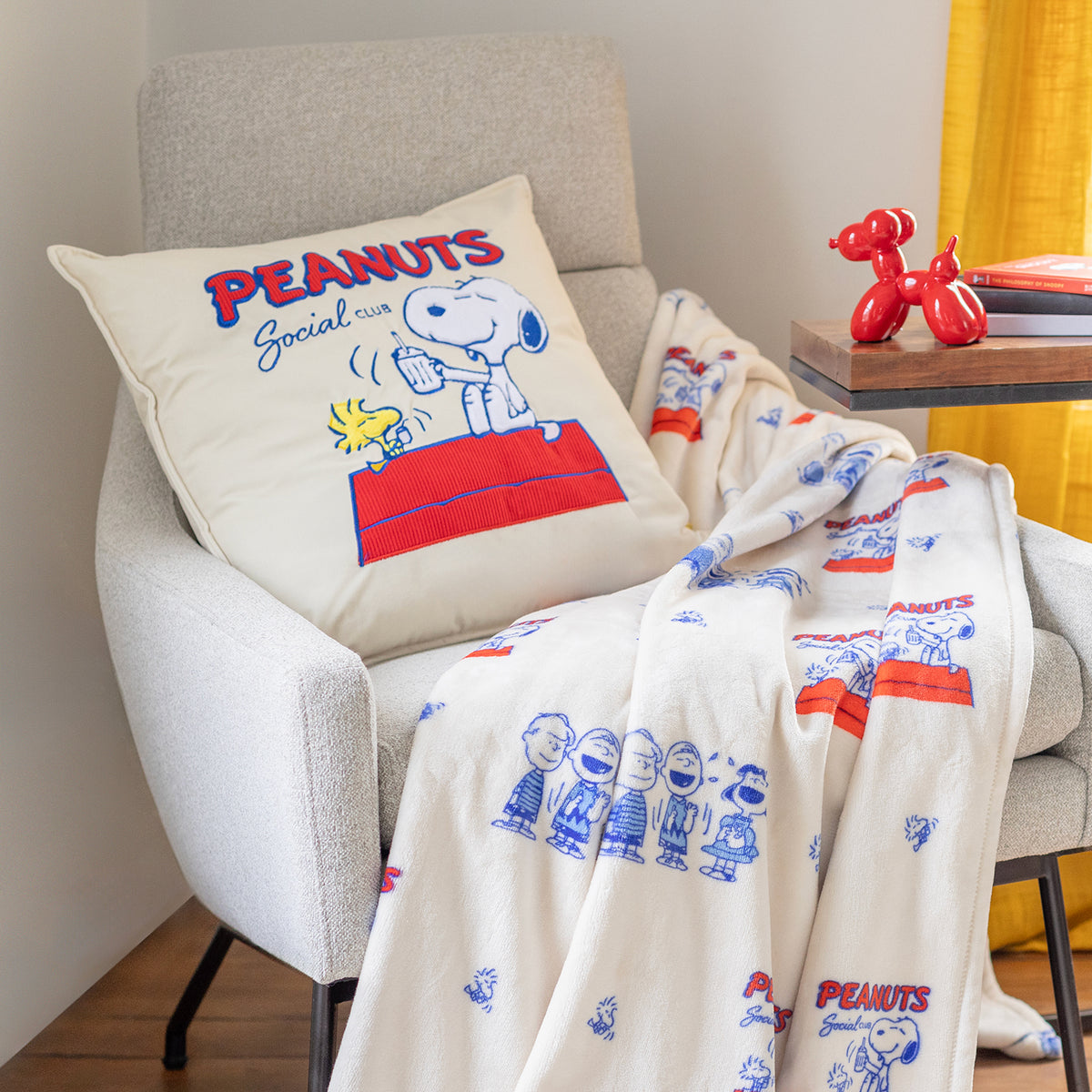 Peanuts social club throw pillow sititng on a chair with a matching throw.