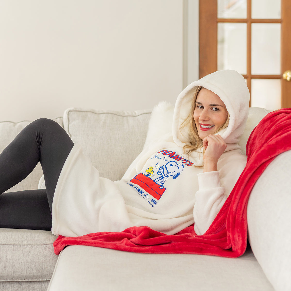 A woman wearing a cream Peanuts lounge hoodie.