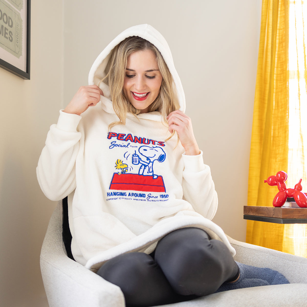 A woman sitting in a chair while wearing a peanuts lounge hoodie.