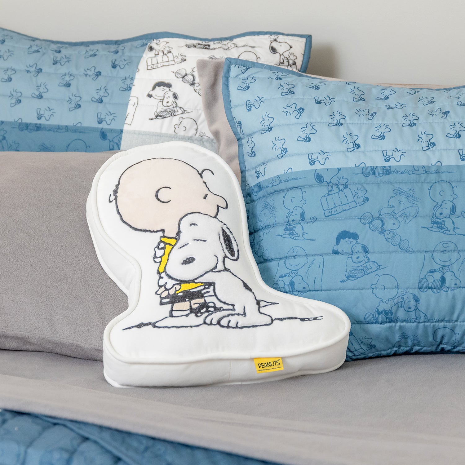Peanuts-themed pillow with cartoon character on a bed with matching bedding.