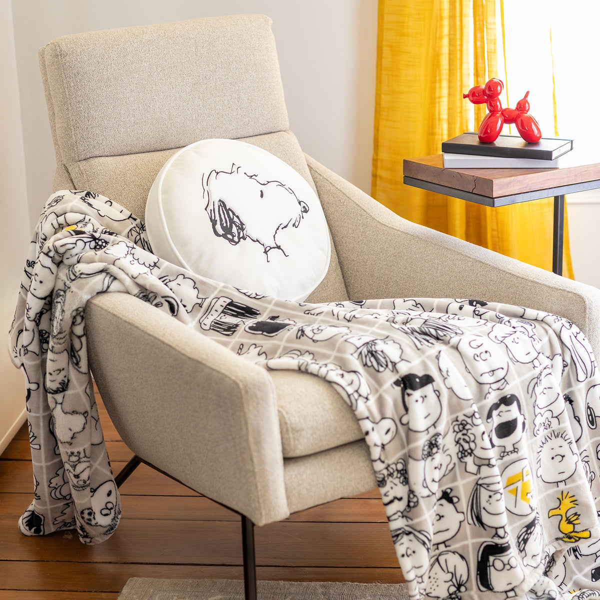 Peanuts 75th Anniversary Throw and Pillow on a beige chair.