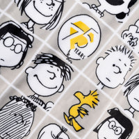 Close up of a Peanuts 75th Anniversary Throw & Pillow Set draped over a brown leather chair.