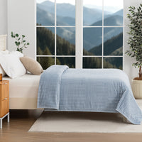 A blue waffle blanket decorated on a bed with a scenic background.