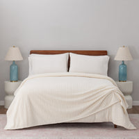 A cream VelvetLoft waffle blanket draped neatly on a white bed.