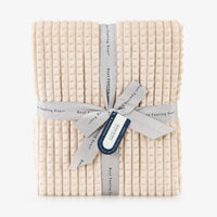 A tan waffle blanket folded neatly on a white surface.