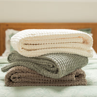 Stack of folded blankets in beige, gray, and brown on a bed.
