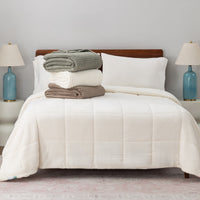 A stack of a green, cream, and brown VelvetLoft waffle blanket on a white bed.