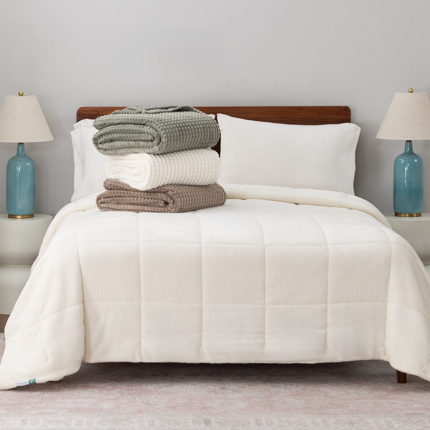 A stack of a green, cream, and brown VelvetLoft waffle blanket on a white bed.