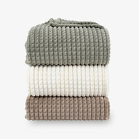 A stack of a green, cream, and brown VelvetLoft waffle blanket on a white surface.