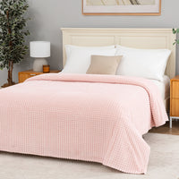 Pink textured blanket decorated neatly on a bed.