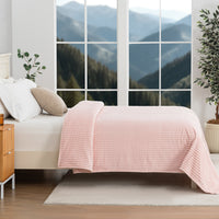 Pink textured blanket decorated neatly on a bed with a scenic background.