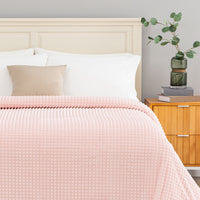 Pink textured blanket decorated neatly on a bed.