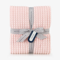 A pink waffle blanket folded neatly on a white surface.
