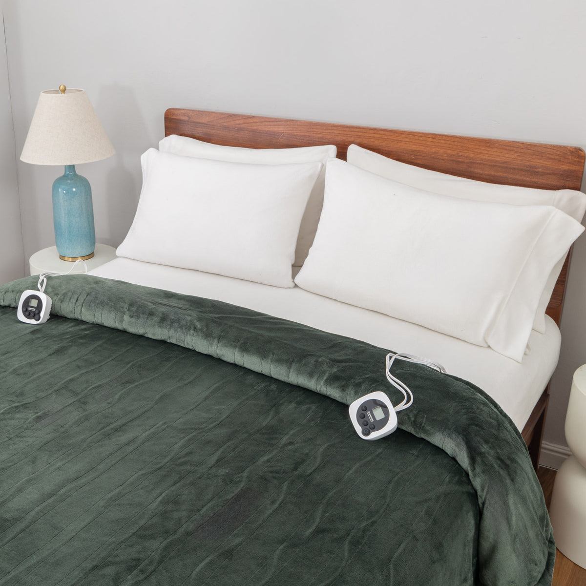 Green heated blanket on a bed with white pillows and a wooden headboard.