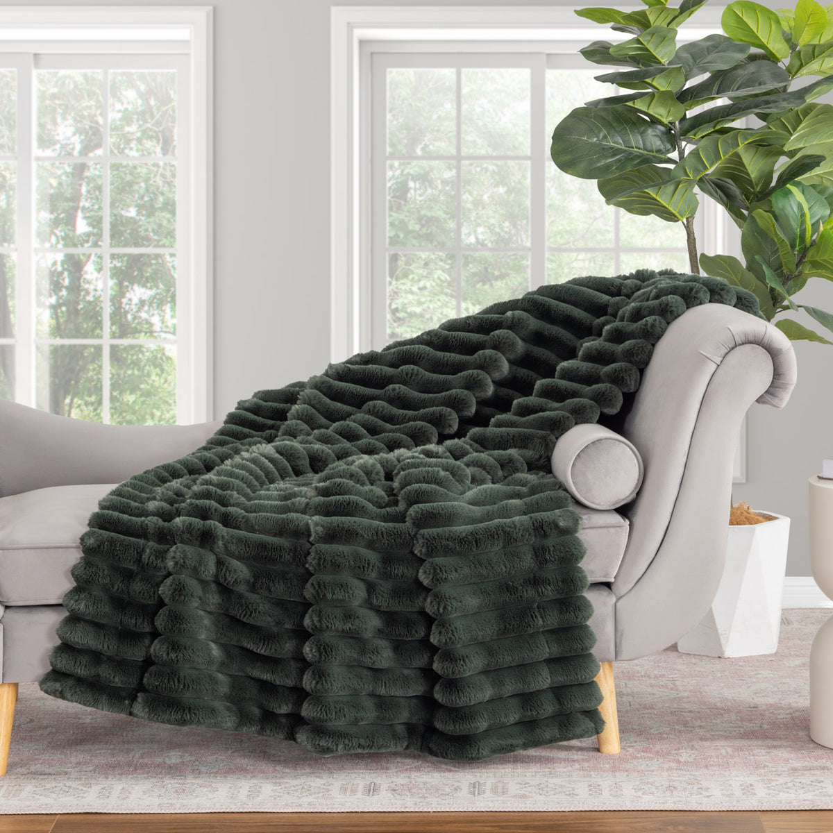 Dark green fluffy blanket draped over a gray sofa in a living room with a plant in the background.