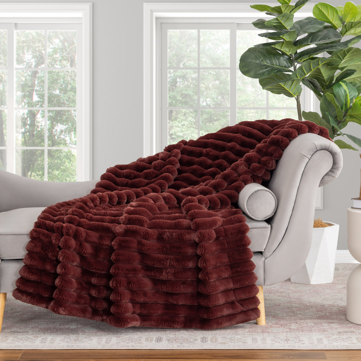 Maroon faux fur throw blanket draped over a gray sofa in a living room.