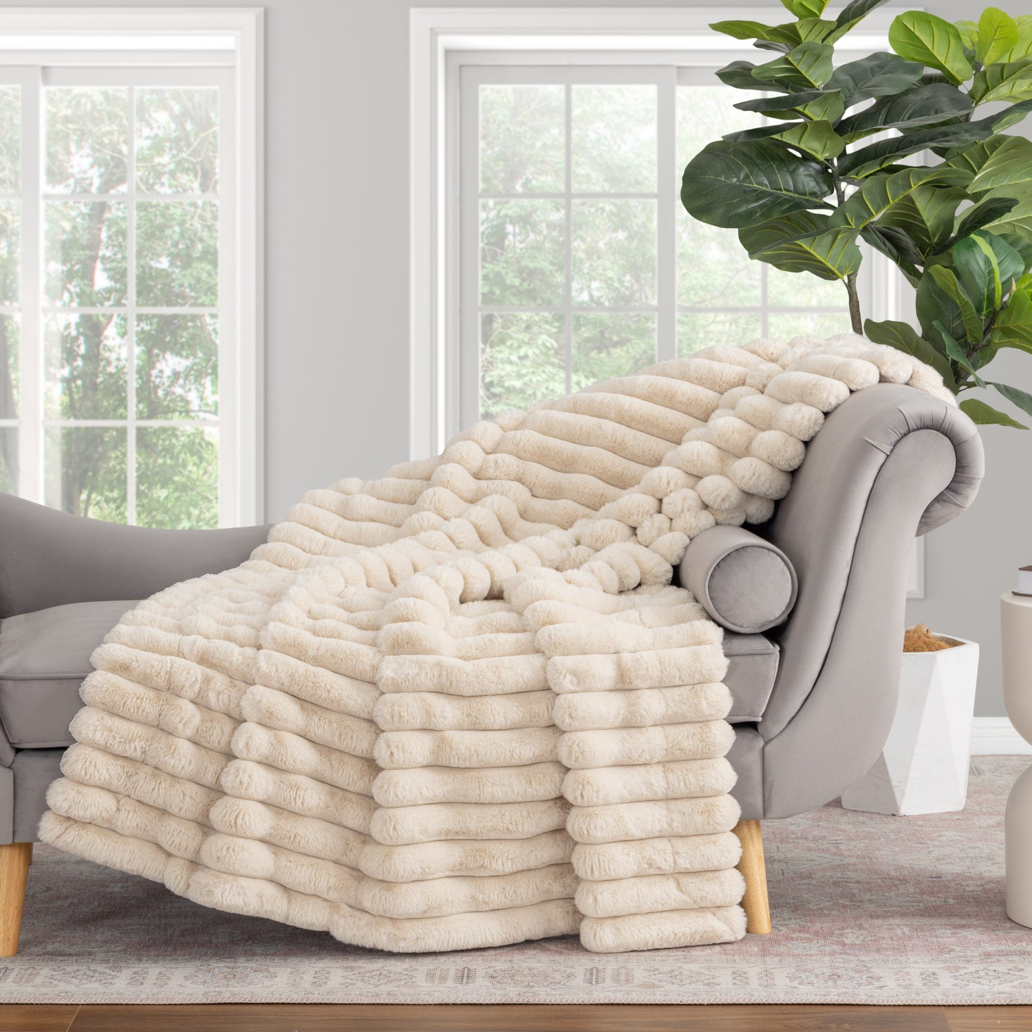 Beige blanket draped over a gray armchair in a room with large windows and a plant.