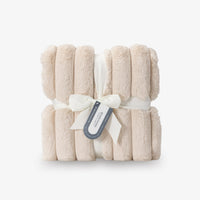 Folded beige blanket with a white ribbon and tag on a light gray background