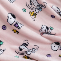 A close-up of a soft pink fabric with an all-over print of Snoopy and Woodstock in black, white, yellow, purple, and teal.