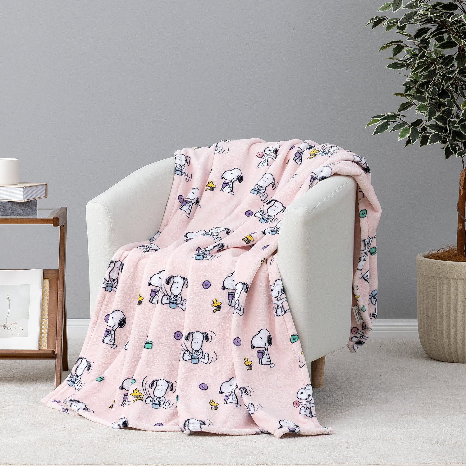 A pink fleece throw blanket with a cartoon dog character print draped over a light gray armchair in a styled room setting.