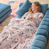 A woman laying on a blue sofa with a pink Peanuts throw blanket draped over her.