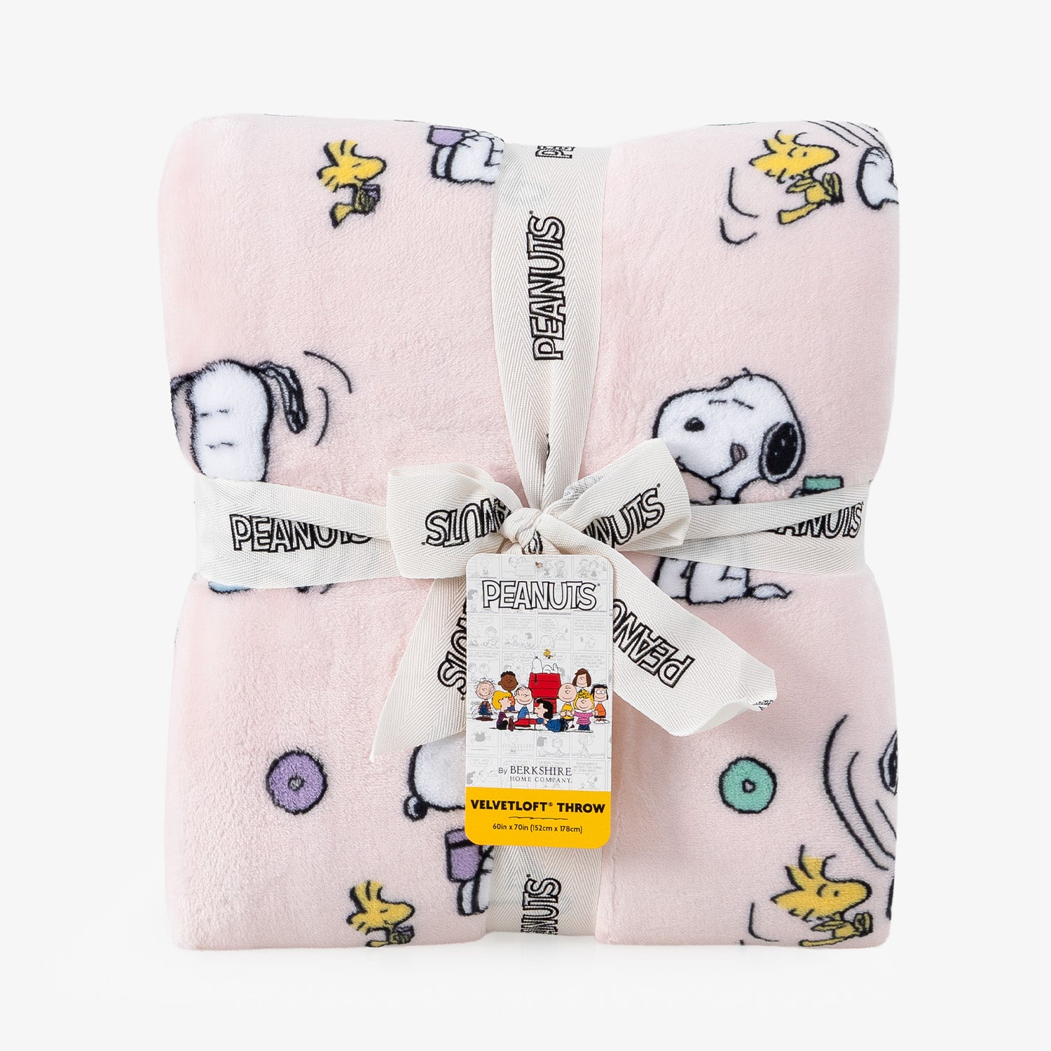 A folded light pink plush blanket with a Peanuts character print, tied with a white ribbon and hangtag. The blanket features Snoopy, Woodstock, and other Peanuts characters on a clean white background.