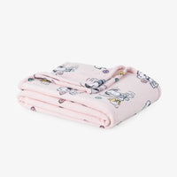 A light pink fleece throw blanket with a cartoon Snoopy and Woodstock print, folded neatly on a white surface.