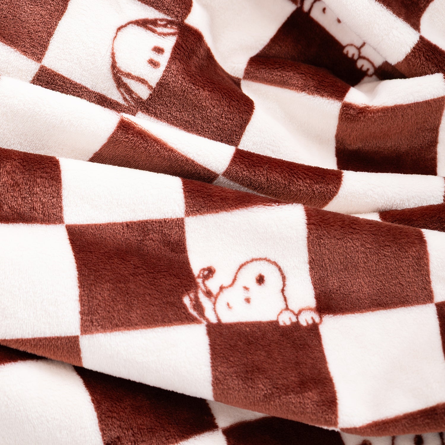 Brown and white checkered plush blanket with cartoon dog peeking out from the squares, shown in a close-up folded view.