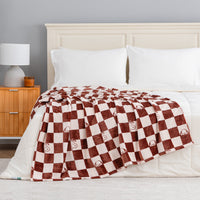 A checkered snoopy throw draped neatly over a white bed.