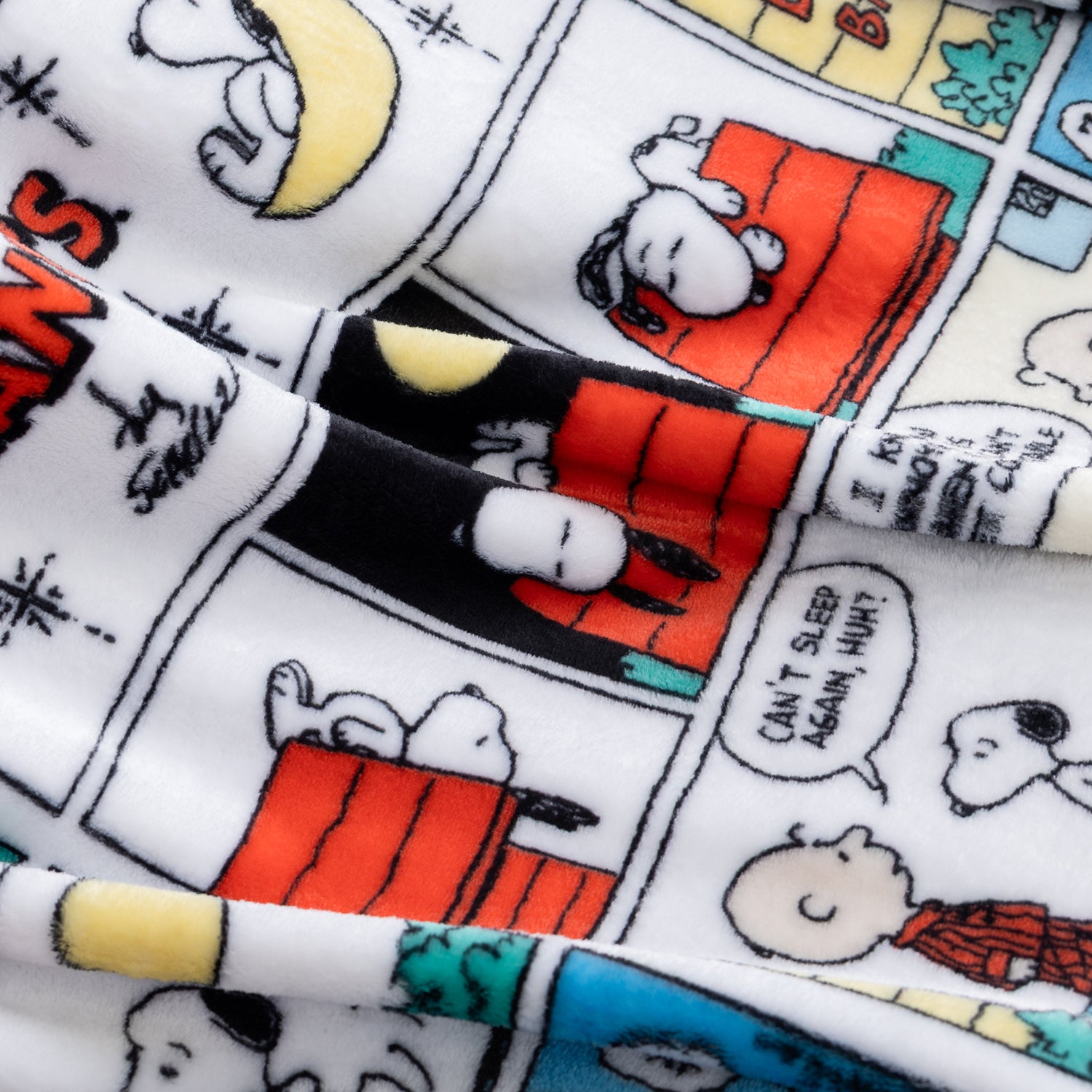 Close-up of a plush blanket featuring a Peanuts comic strip print with Snoopy and Charlie Brown, showing the soft fabric texture and colorful comic panels.