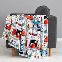 A fleece throw blanket featuring a classic Peanuts comic strip print draped over a dark gray armchair.