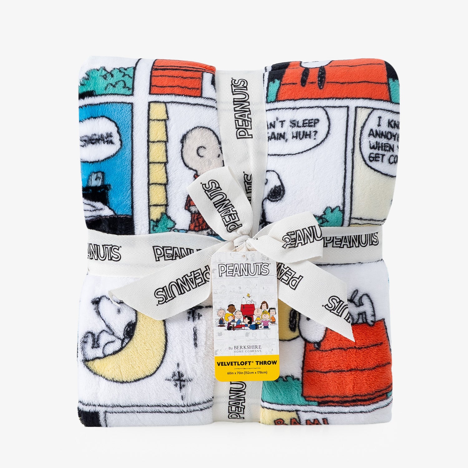 A folded plush throw blanket featuring Peanuts comic strip characters and scenes, tied with a white branded ribbon and a small yellow care tag, on a light gray background.