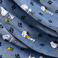 A close-up of a blue plush fabric featuring a repeating pattern of the Peanuts characters Snoopy, Woodstock, and black paw prints.