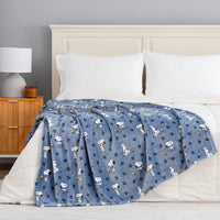 A blue blanket with a repeating cartoon dog print is draped over a bed with white bedding in a bedroom setting.