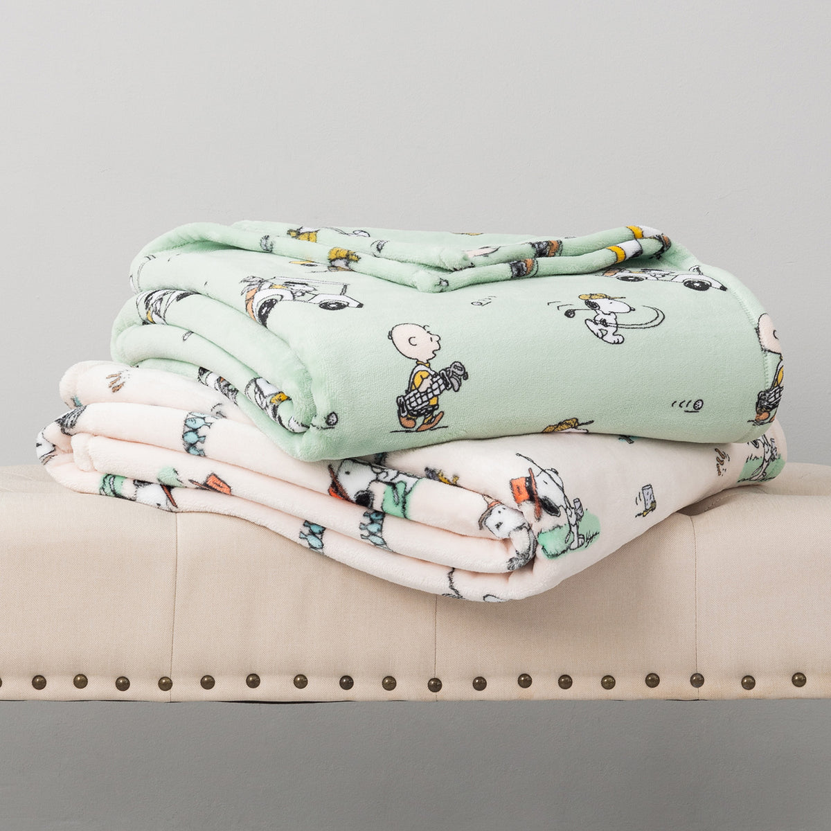 Stack of cartoon-themed blankets on a beige couch with a gray background
