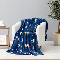 A navy blue plush throw blanket with a repeating cartoon character print is draped over a white armchair in a styled room setting.